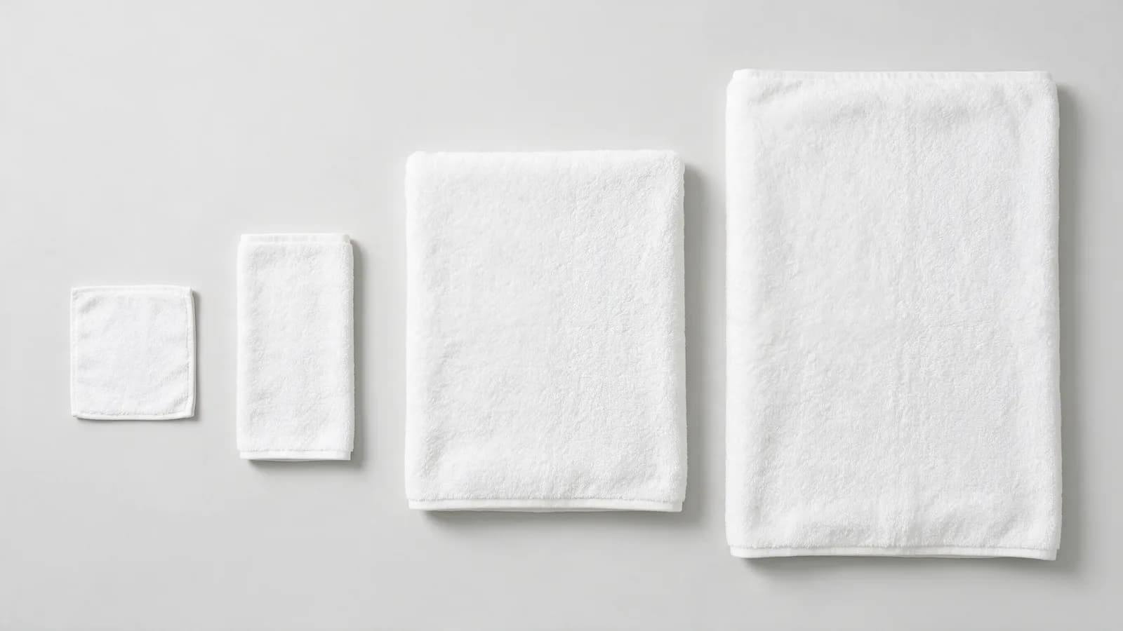 A washcloth, hand towel, bath towel and bath sheet laid flat and overlapping, photographed from above, showing the size difference between each piece