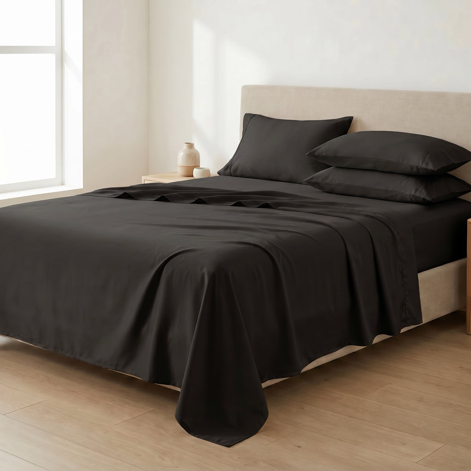 Black Egyptian cotton sateen sheet set on a queen bed with the flat sheet folded back and matching pillowcases in a minimal luxury bedroom